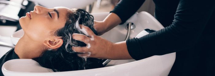 Woman applying shampoo and massaging hair of a customer. Woman having her hair washed in a hairdressing salon.